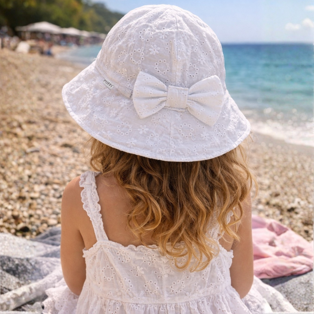 Deklica na plaži nosi bel čipkast klobuček z mašno blagovne znamke Puffi, idealen za zaščito pred soncem